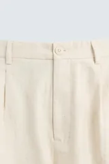 Pantalón de corte recto, color beige claro, con pliegues frontales y bolsillos de vivo en la parte trasera.