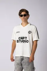 Remera tejida color crudo con cuello tipo chomba en V, mangas cortas con rayas negras y estampado con letras en el frente. Confeccionada en hilado de algodón.