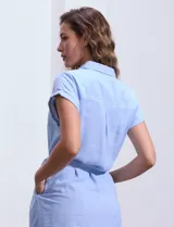 Vestido camisero corto con estampado de rayas verticales celestes y blancas. Tiene cuello camisero, mangas cortas con dobladillo, cierre frontal con botones y cinturón de lazo en la cintura.