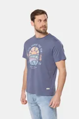 Remera blanca de manga corta con cuello redondo y un estampado gráfico frontal que simula un paisaje costero con un sol naciente o poniente, rodeado por texto circular que dice "SURF - LIFE UNDER THE SUN - CLUB".