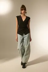 Top negro sin mangas, con escote en V cruzado y detalle de botones laterales. Presenta un corte ajustado al cuerpo con un diseño asimétrico en el ruedo.