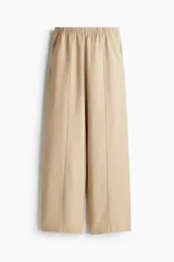 Pantalón color beige de lino con tiro alto, cintura elástica, bolsillos al bies y bolsillos traseros insertados. Piernas rectas con pliegue cosido adelante.