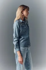 Camisa de denim celeste con apliques de piedras plateadas en los hombros, corte recto, cuello camisero, botones metálicos y bordado Rapsodia en la espalda.