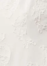 Vestido corto blanco con textura, tirantes finos y espalda abierta con lazo. Tiene escote de pico, cierre de cremallera en la parte posterior y corte globo.