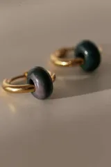 Par de aros tipo argolla dorados con dije de piedra natural con patrón de manchas negras sobre fondo blanco.