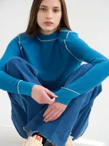 Polera negra de tela rib con cuello alto y mangas largas. Presenta pespuntes rojos en cuello, hombros y puños.