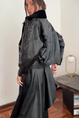 Campera bomber negra de cuero con cuello de piel sintética negra, forro interior y detalles de pasamanería en cuero marrón gastado en las mangas.