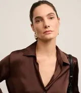 Camisa blanca de satén con cuello inglés, manga larga y cierre frontal con botones.