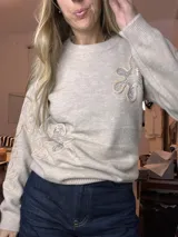 Suéter de tejido de punto color beige claro, con cuello redondo y puños y ruedo acanalados. Presenta apliques florales en relieve con lentejuelas plateadas en el frente y en las mangas.