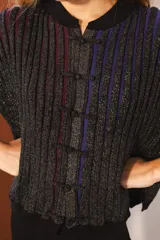 Cárdigan tejido con lurex, con cuello redondo, manga 3/4 y cierre frontal con botones forrados. Diseño con rayas verticales en tonos verde, azul y violeta sobre fondo negro con brillo.