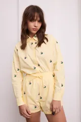 Camisa amarilla con bordado de flores rojas, de corte recto y manga larga.