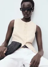 Chaleco color crema con cuello redondo y cierre frontal con botones.