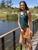 Musculosa de cuero verde con cuello redondo tejido en crochet color crema y apliques de flores blancas. Presenta flecos largos en los laterales y espalda tejida.