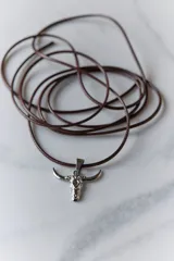 Dije plateado con forma de cráneo de toro con orificio en la frente.