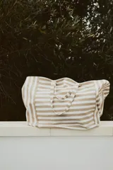 Bolso de playa tipo tote bag, de lona de algodón a rayas horizontales color beige y blanco. Tiene doble asa de hombro y un compartimento interior.