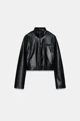 Cazadora corta negra de efecto piel, con cuello subido y manga larga. Tiene bolsillos delanteros con cremallera metálica y cierre frontal con cremallera.