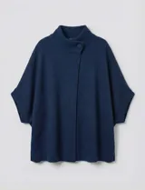 Capa o poncho tejido color verde esmeralda, con cuello polera alto que se cierra con un botón grande en el lateral. Presenta mangas cortas estilo japonesa y un calce amplio.