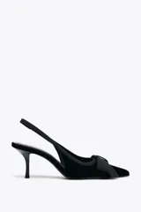 Zapato destalonado negro de terciopelo con tacón fino y tira trasera elástica. Detalle de lazo en la parte delantera.