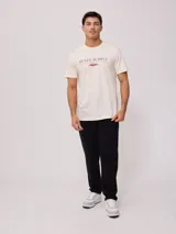 Remera color crema de manga corta con estampado frontal con el texto "Rusty Supply Surfboards" en color rojo y negro.