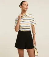 Short color beige de cintura alta, confeccionado en tejido plano con estructura sastre, con bolsillos laterales con tachuelas metalizadas.