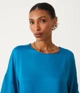 Blusa celeste de viscosa con textura satinada, cuello redondo, manga corta con sisa desplazada y abertura en la espalda.
