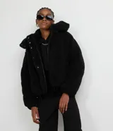 Campera puffer de sherpa color negro, con capucha, cierre frontal y regulador elástico en la cintura.