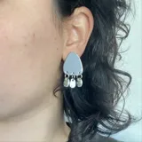 Par de aros colgantes plateados con forma triangular y tres dijes redondos colgando de la base.