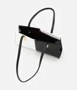 Cartera shoulder mediana de cuero sintético, con diseño bicolor blanco y negro y detalles metálicos dorados.