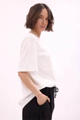 Remera blanca de algodón, corte oversize, con cuello redondo y manga corta. Presenta un estampado frontal con varias reposeras y hamacas de playa, y el texto "LA SIESTA".