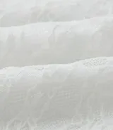 Blusa de manga larga confeccionada en tejido de laise blanco, con cuello redondo, volados frontales y mangas acampanadas.