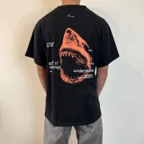 Remera negra de algodón con estampado de un tiburón en color naranja y tipografía en blanco.