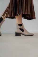 Botines Chelsea color beige con elásticos laterales negros, punta cuadrada, detalle de hebilla lateral y tacón bloque bajo.