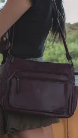 Cartera de cuero color borgoña, con correa larga regulable, dos bolsillos frontales con cierre y un bolsillo trasero con cierre.