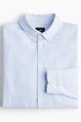 Camisa de vestir celeste y blanco a rayas verticales, de corte regular fit, con cuello abotonado, bolsillo en el pecho y mangas largas con puños abotonados.