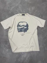 Remera beige de algodón con cuello redondo y estampado frontal de un rostro en tonos grises y texto "FUTUREPROOF".