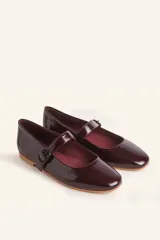 Zapato tipo Mary Jane de charol color borgoña, con punta redondeada, tira sobre el empeine con hebilla y suela de cuero.