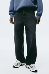 Jean negro de denim de algodón rígido, corte holgado de cadera a bajo con piernas redondeadas extraamplias y pliegues al tobillo. Cintura clásica con cierre y tiro bajo.