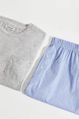 Conjunto de pijama para hombre, compuesto por una remera gris de manga corta con bolsillo en el pecho y un short a rayas verticales celestes y blancas con cintura elástica y botones decorativos.