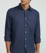 Camisa marrón claro de lino, de corte clásico, con cuello inglés, manga larga y cierre frontal con botones blancos.