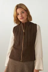 Chaleco color crema con cuello alto y cierre frontal con cremallera. Diseño con alforzas verticales en la parte superior delantera y trasera.