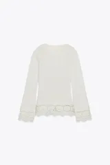 Camiseta blanca de manga larga con cuello redondo y detalle de encaje en el ruedo y puños.