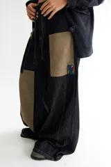 Pantalón de jean negro de corte acampanado, con parches de pana color visón y cordones en la cintura.
