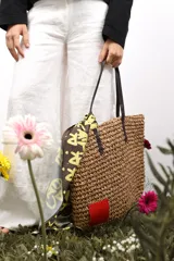 Bolso de rafia color beige con asas de cuero marrón y parche de cuero rojo en una esquina.