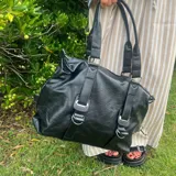 Bolso tipo tote de eco cuero negro con doble asa de hombro y cierre superior.