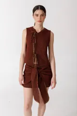 Top sin mangas color ladrillo, tejido en punto arroz con textura suave. Presenta un corte recto y lazos finitos decorativos en el frente, simulando una abertura.