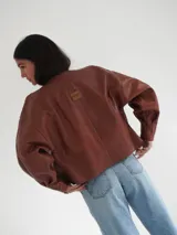 Campera oversize de cuero color marrón con cierre frontal y detalles de costuras en los bordes.
