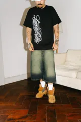 Bermuda baggy de jean con lavado verde, bordado en negro y rojo, cierre y botón personalizado, corte amplio y bolsillos grandes.