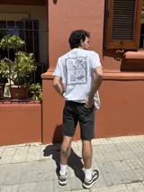 Camiseta blanca de manga corta con estampa en la espalda de una escena de playa enmarcada.