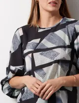 Blusa de gasa estampada con flores verdes sobre fondo blanco, de la marca Sioni. Tiene mangas cortas amplias con abertura y botón.