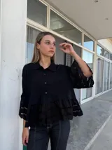 Camisa negra con cuello clásico, cierre frontal con botones, mangas 3/4 con detalle de calado y ruedo con volados y calado.